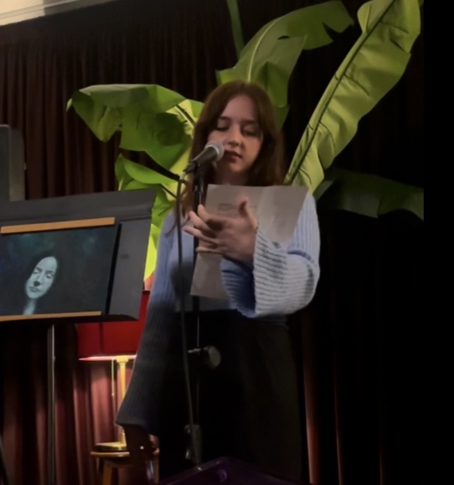Carissa Rees reading her poetry into a microphone in low light.